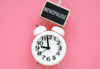 Relógio com uma placa indicando período de menopausa, em um fundo rosa.