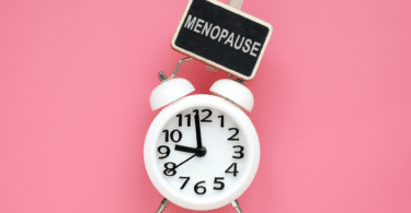 Relógio com uma placa indicando período de menopausa, em um fundo rosa.