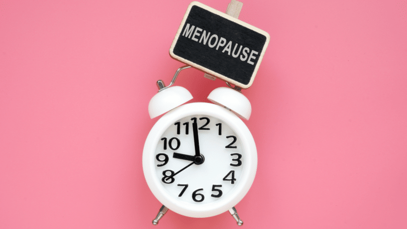 Relógio com uma placa indicando período de menopausa, em um fundo rosa.