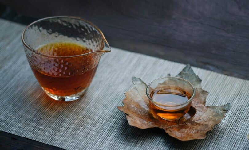 Jarra e xícara com chá. A xícara está sobre uma folha seca.