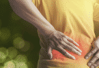 Mulher com a região do cóccix em vermelho com as mãos pressionadas no local