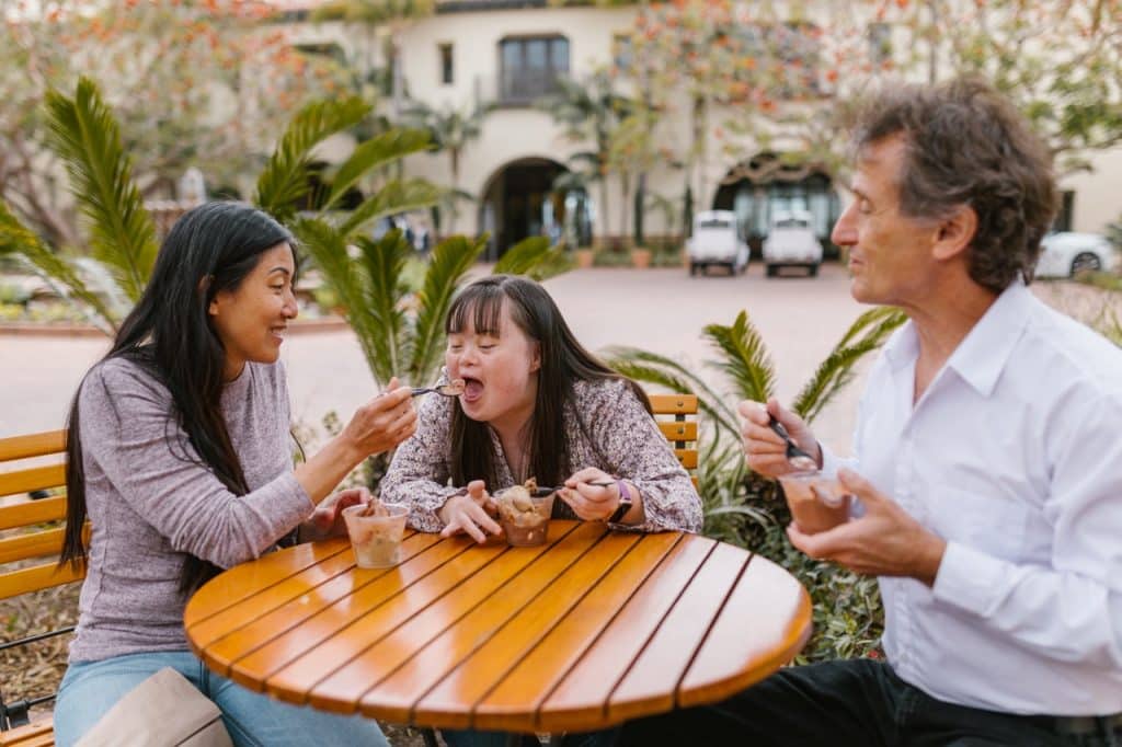 Menina autista sentada na mesa comendo com os pais. 