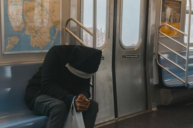 Homem sentado no metrô, com a cabeça baixa.