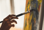 Na imagem, há o foco na mão de uma pessoa pintando um quadro.