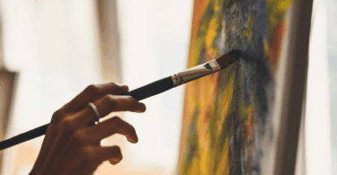 Na imagem, há o foco na mão de uma pessoa pintando um quadro.