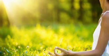 Braço de mulher meditando com fundo verde e sol refletindo