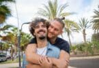 Casal gay abraçado em uma rua que parece de praia