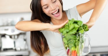 Mulher sorrindo, empurrando muitas folhas dentro de um liquidificador.