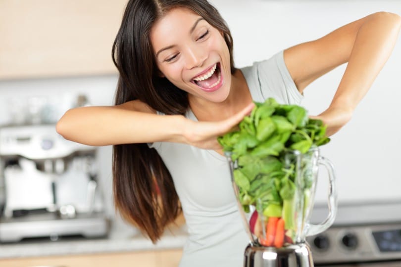 Mulher sorrindo, empurrando muitas folhas dentro de um liquidificador.