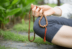 Pessoa meditando sentada na grama segurando um colar de contas