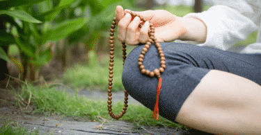 Pessoa meditando sentada na grama segurando um colar de contas