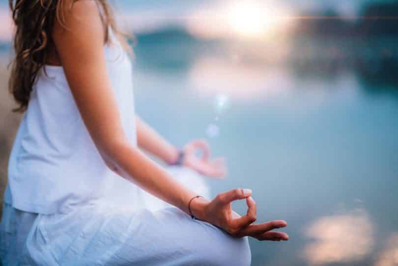 Mulher meditando próxima de um lago.