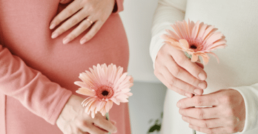 Mulher grávida segurando uma margarida rosa.