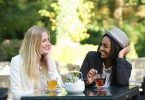 Duas mulheres sorridentes tomando chá em meio à natureza.