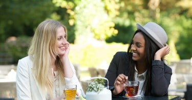 Duas mulheres sorridentes tomando chá em meio à natureza.