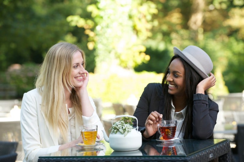 Duas mulheres sorridentes tomando chá em meio à natureza.