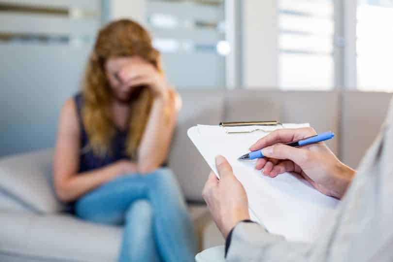 Psicóloga conversando com seu paciente deprimido e fazendo anotações no consultório