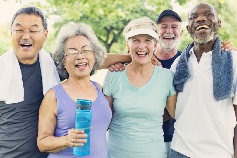 Grupo de idosos em um parque, sorrindo, com roupas de ginástica.