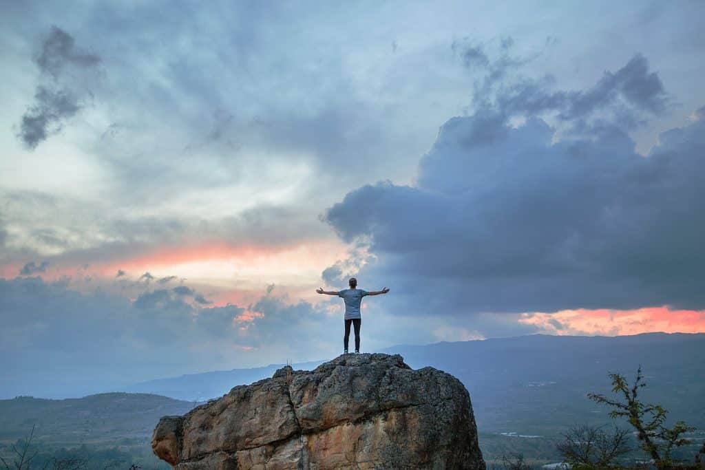 Homem em cima de uma montanha com os brços abertos olhando para o horizonte