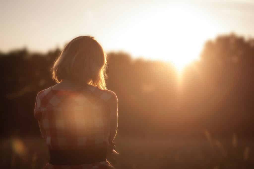 Mulher olhando para o sol entre as árvores