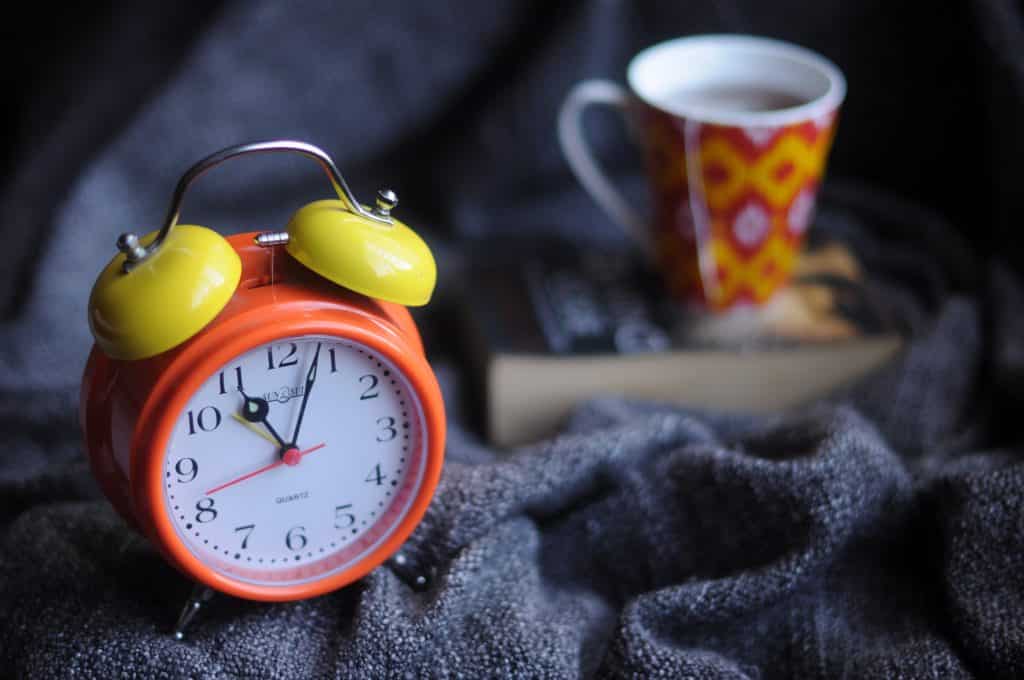 Relógio na cama ao lado de uma xícara de chá com um livro