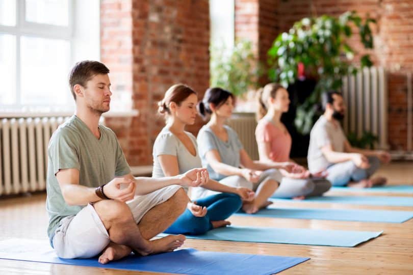 Grupo de pessoas meditando em uma sala, lado a lado.