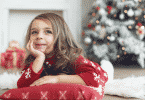 Menina deitada no chão com pijama de Natal. Ao fundo, decorações natalinas