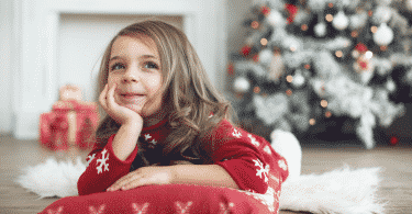 Menina deitada no chão com pijama de Natal. Ao fundo, decorações natalinas