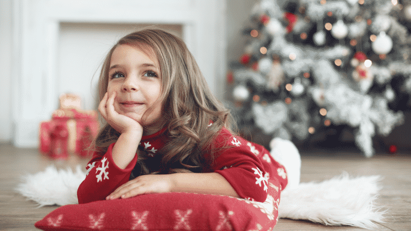 Menina deitada no chão com pijama de Natal. Ao fundo, decorações natalinas