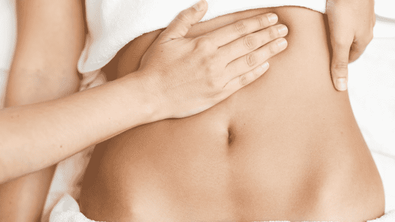 Mulher deitada recebendo massagem no abdomen