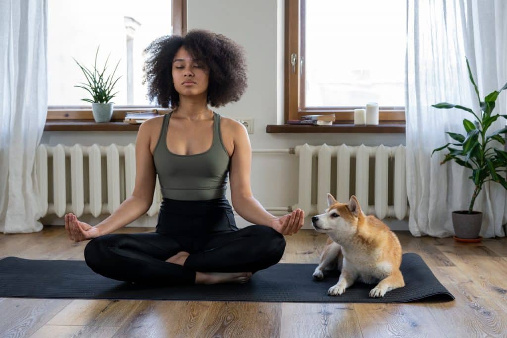 Mulher sentada no chão ao lado de seu cachorro, meditando.