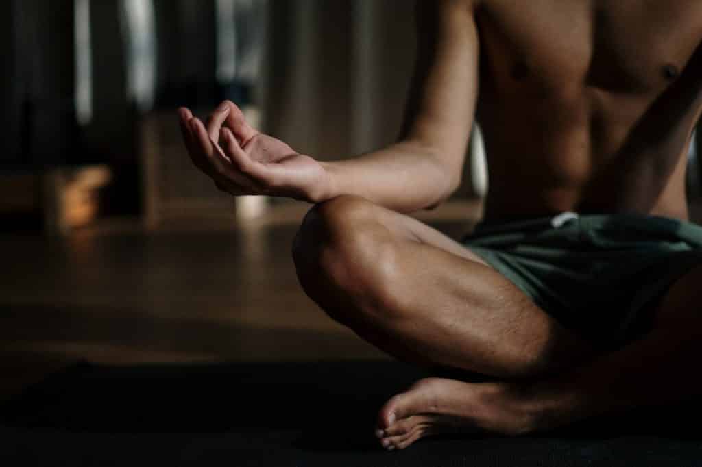 Homem sentado no chão, sem camisa, meditando.