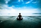 Mulher sentada em pose de meditação em frente ao mar.