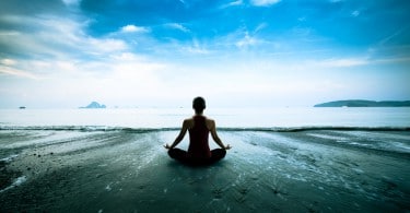 Mulher sentada em pose de meditação em frente ao mar.