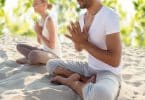 Duas pessoas sentadas na areia, de pernas cruzadas, meditando.