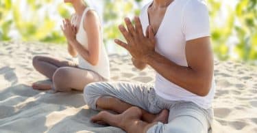 Duas pessoas sentadas na areia, de pernas cruzadas, meditando.