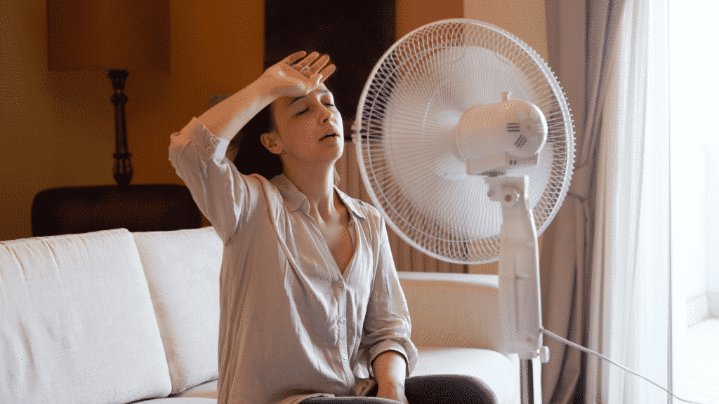 Mulher suando sentada na frente do ventilador
