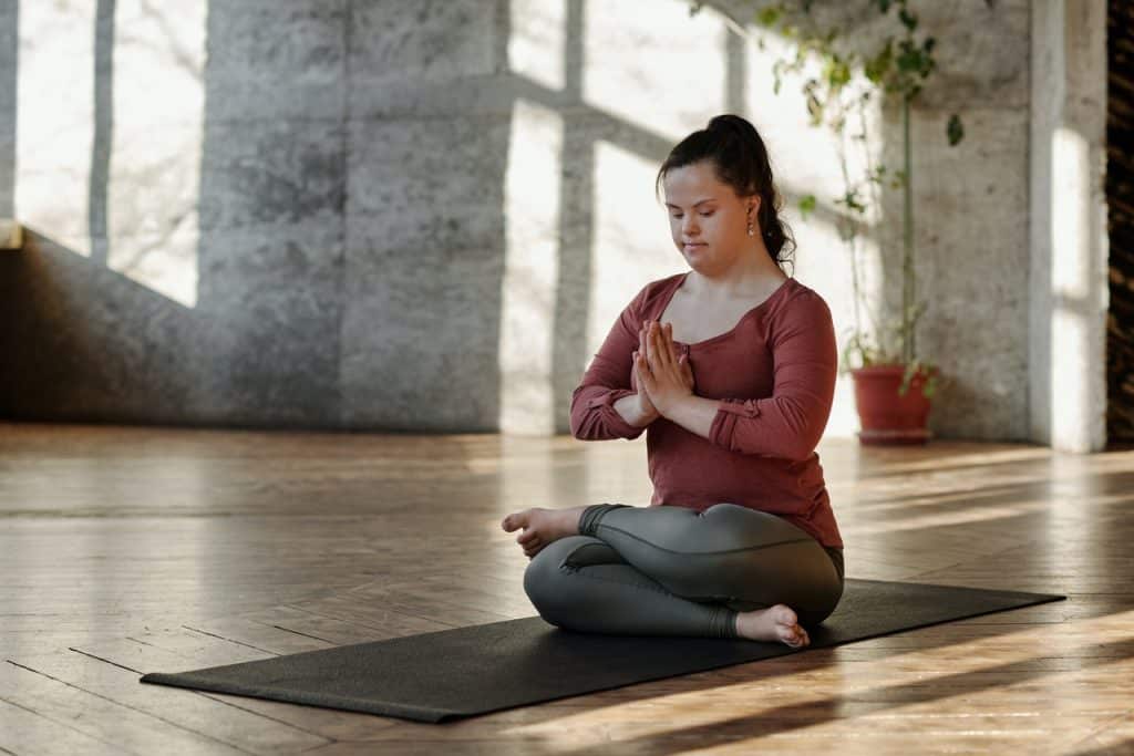 Mulher sentada. de pernas cruzadas e olhos fechados, meditando.