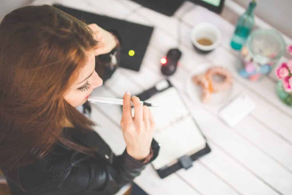 Mulher com uma caneta na boca em usa mesa de estudo