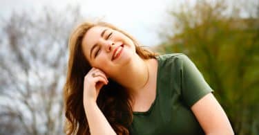 Mulher branca sorrindo de olhos fechados.