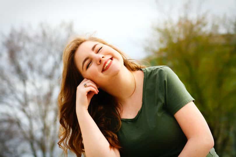 Mulher branca sorrindo de olhos fechados.