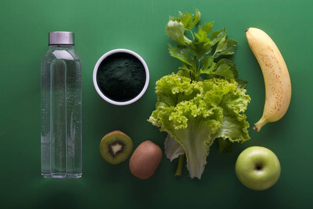 Diversas frutas ao lado de uma garrafa de água e de um potinho com tempero