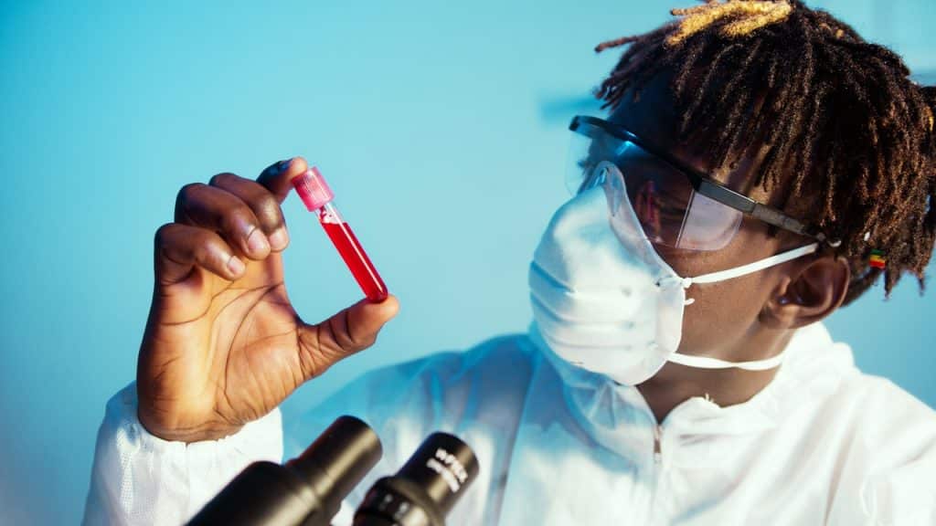 Homem com máscara e óculos segurando um tubinho com sangue.