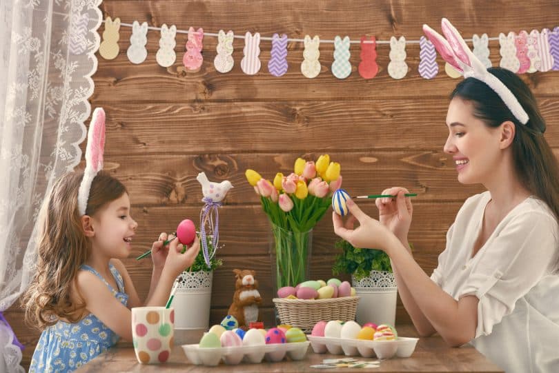 Uma mãe e sua filha usando orelhas de coelho pintando ovos de Páscoa.