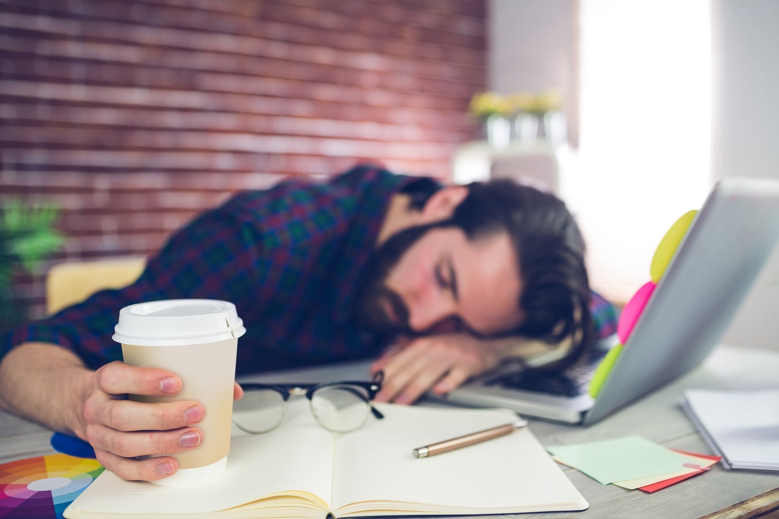 Tired creative editor holding disposable cup while sleeping on o