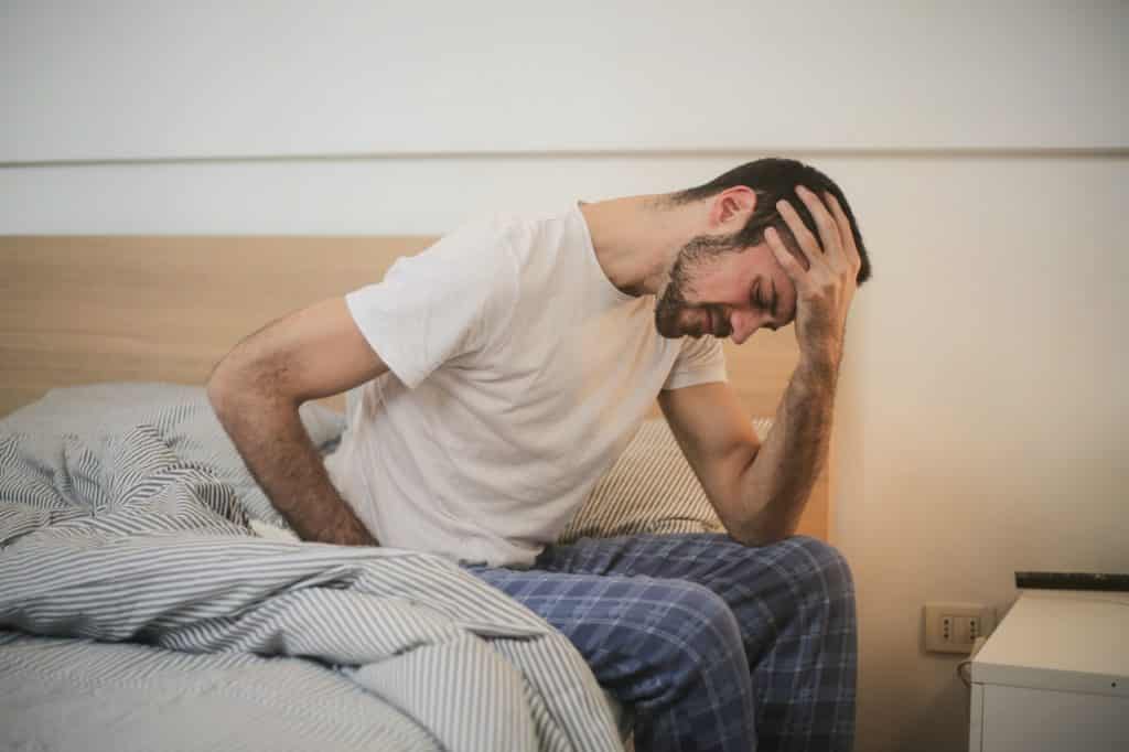 Homem sentado na cama com a mão sobre a cabeça.