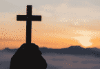 Silhueta de mãos segurando uma cruz durante o pôr do sol