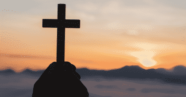 Silhueta de mãos segurando uma cruz durante o pôr do sol