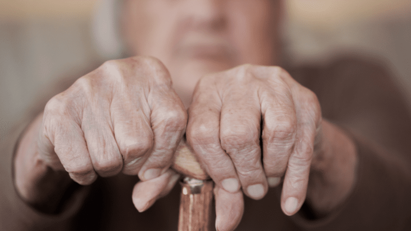 Mãos de pessoa idosa segurando muleta.