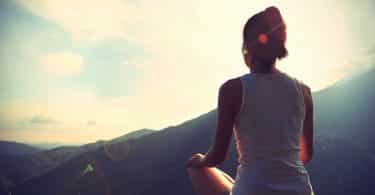 Mulher sentada em uma montanha em direção ao sol